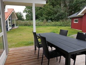 A covered outdoor area with a table and chairs, a wooden deck, and a view of a red building and a house with a red roof. - 4 Star Holiday Home in Grossenbrode (Grossenbrode)