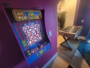 Ein Retro-Spielautomat mit einem Labyrinthspiel, ein Tischfußballtisch und eine Pflanze im Hintergrund.