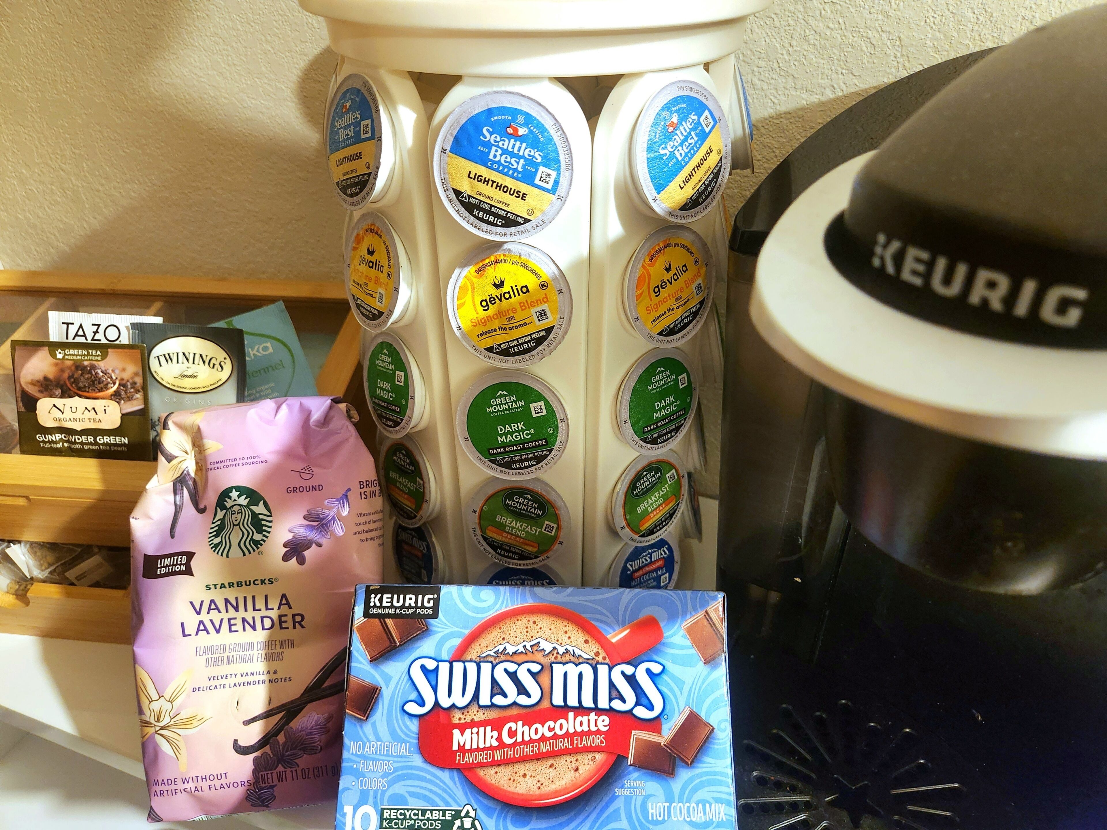A coffee maker, various coffee pods, a Starbucks bag, and a Swiss Miss milk chocolate packet.