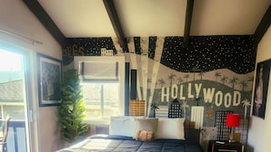 Un dormitorio con cama, mesita de noche, lámpara, ventana y un mural en la pared.