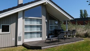 A modern house with a large sliding glass door, a covered patio with outdoor furniture, and a chimney. - 4 Star Holiday Home in Grossenbrode (Grossenbrode)