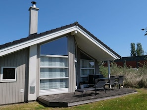 A modern house with a large sliding glass door, a covered patio with outdoor furniture, and a chimney. - 4 Star Holiday Home in Grossenbrode (Grossenbrode)