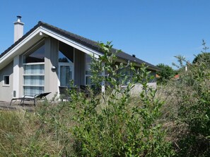 A modern house with large windows, a chimney, and a garden with shrubs. - 4 Star Holiday Home in Grossenbrode (Grossenbrode)