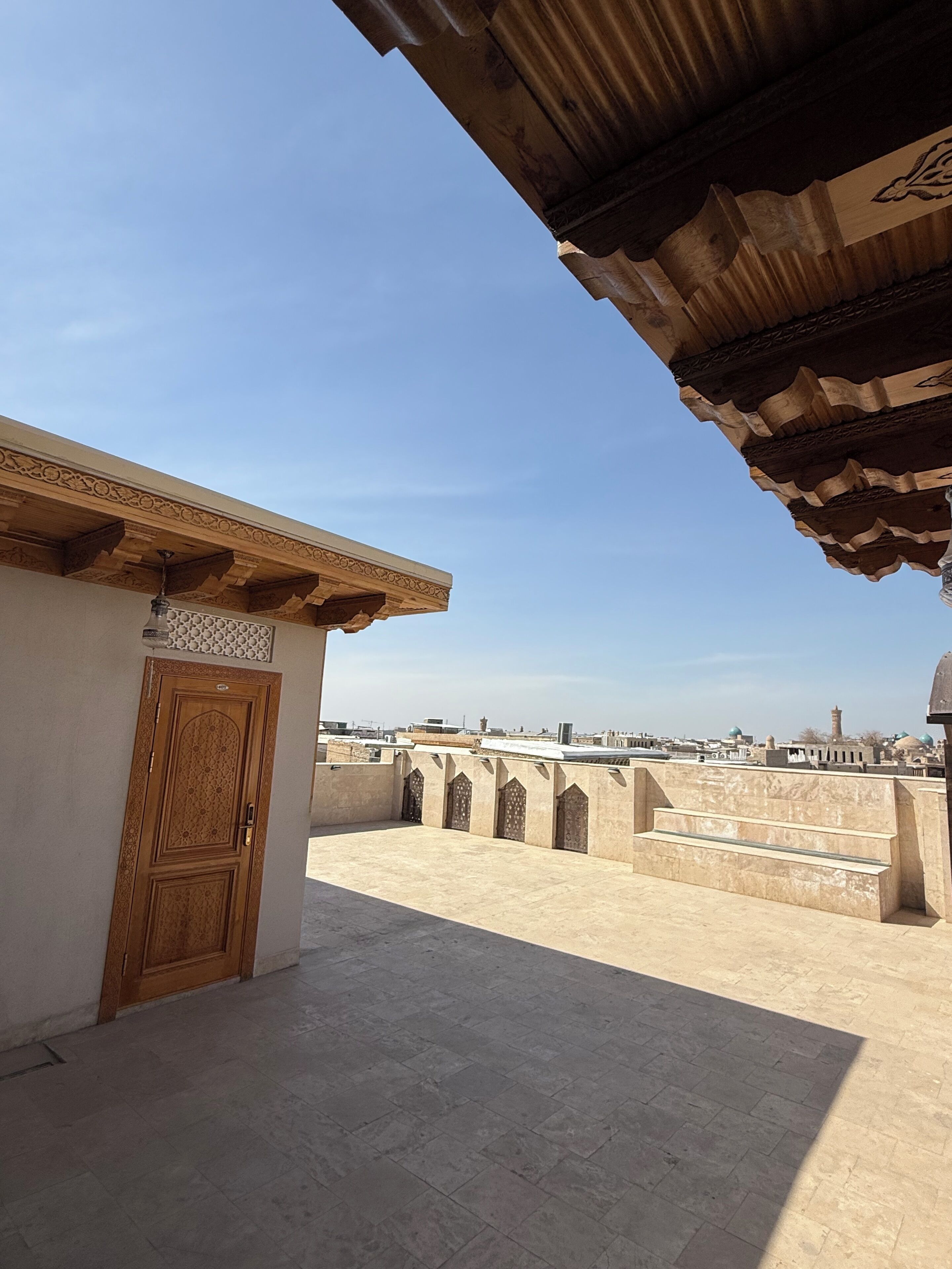 Una terraza en la azotea con una puerta de madera, piso de baldosas y vista de la ciudad.