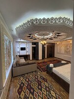 Una habitación amplia con una cama grande, un sofá, un tapete estampado y un diseño de techo elaborado.