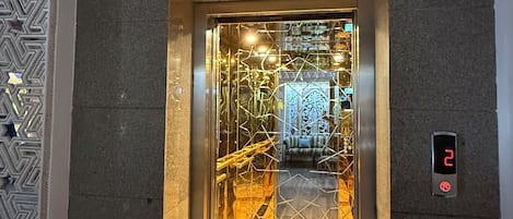 An elevator with a digital display, marble flooring, and a patterned wall.