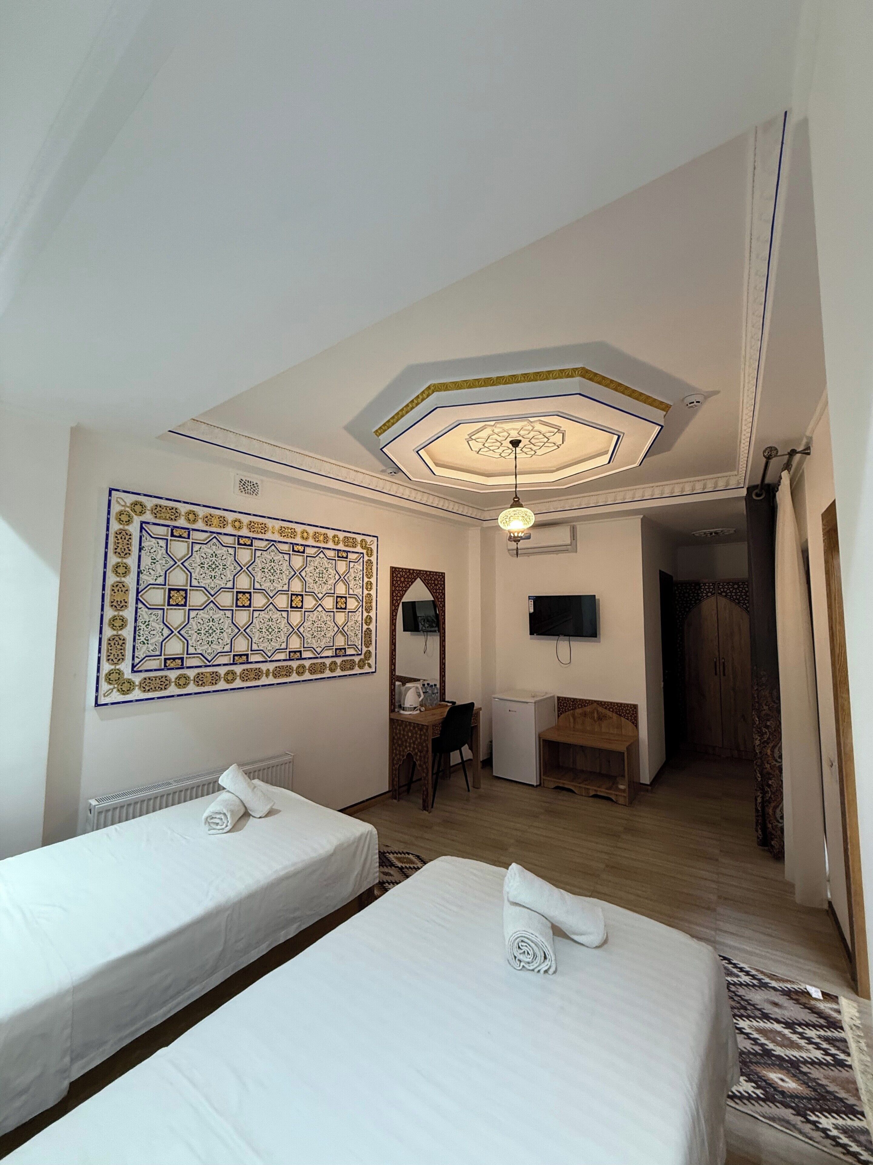 A hotel room with two beds, a desk, a TV, and a decorative ceiling.