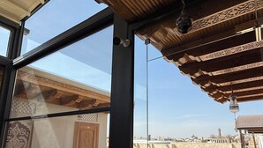 Ein Zimmer mit großem Fenster, Holztür und Blick auf einen Innenhof mit traditioneller Architektur.