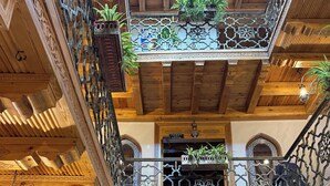 A multi-level interior with ornate wooden balconies, a chandelier, and a sign indicating a restaurant. - Mehrob Hotel (Bukhara)