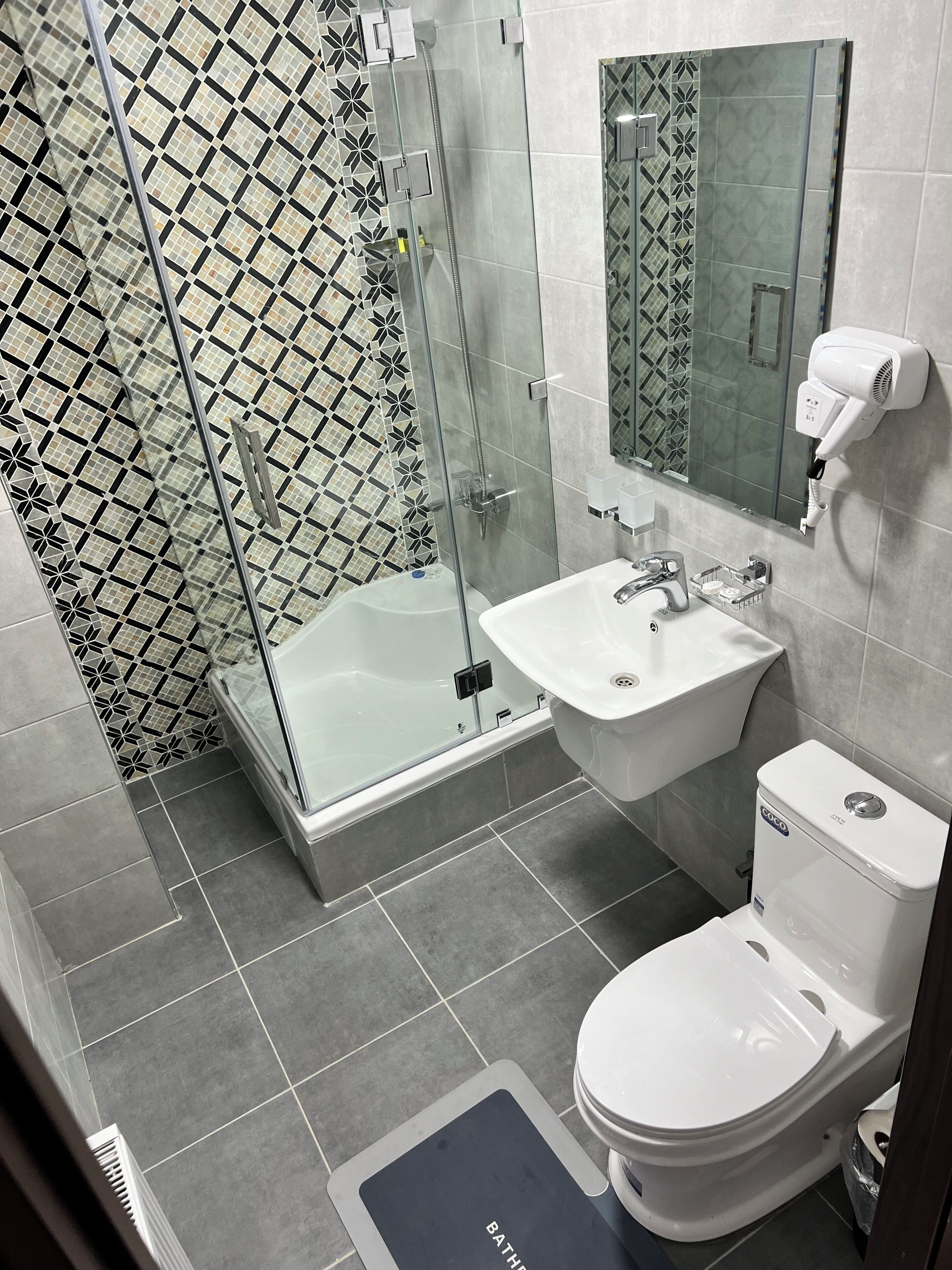 Et moderne badeværelse med brusekabine med glasvægge, en hvid vask, toilet og spejl.