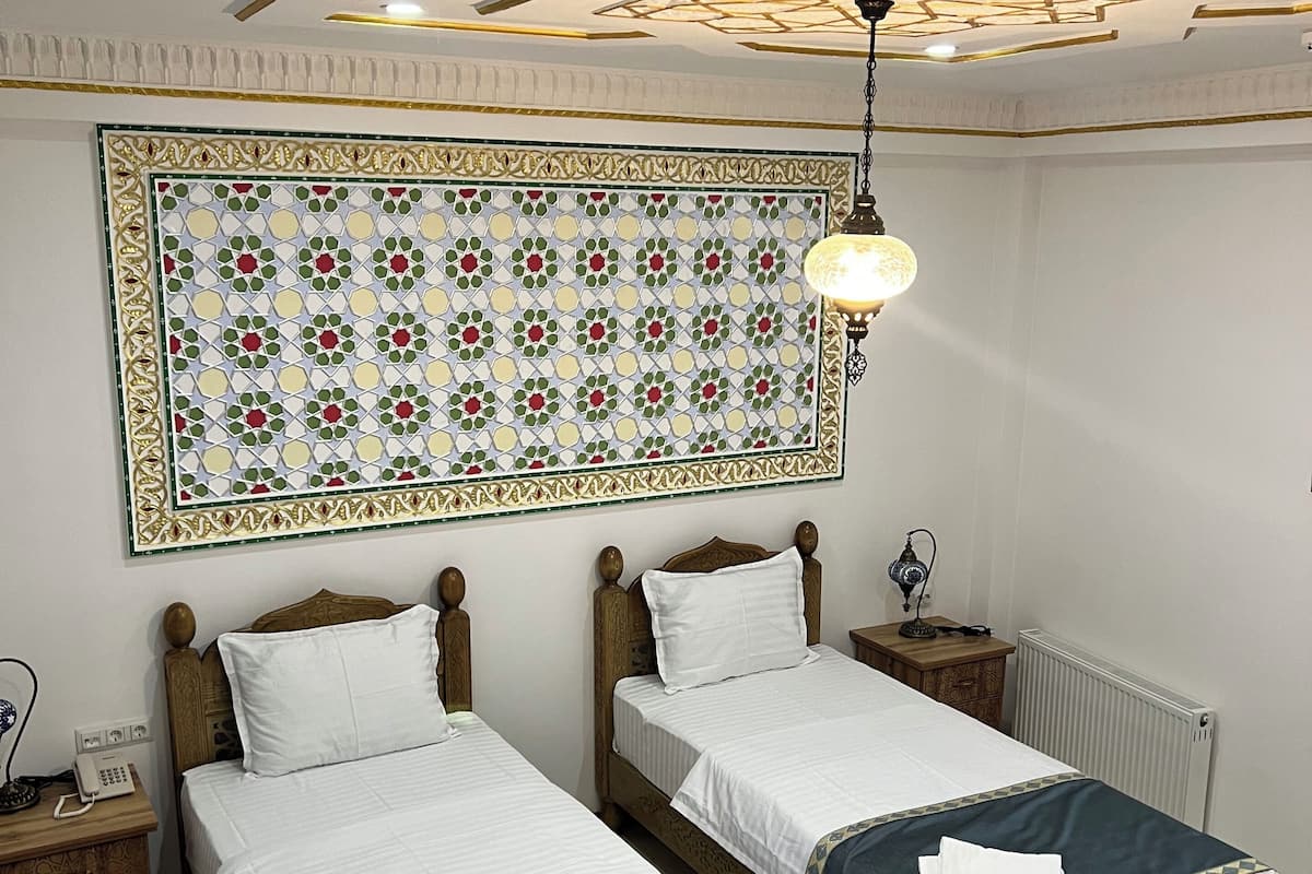 A hotel room with two wooden beds, a patterned headboard, a ceiling light, and a radiator.