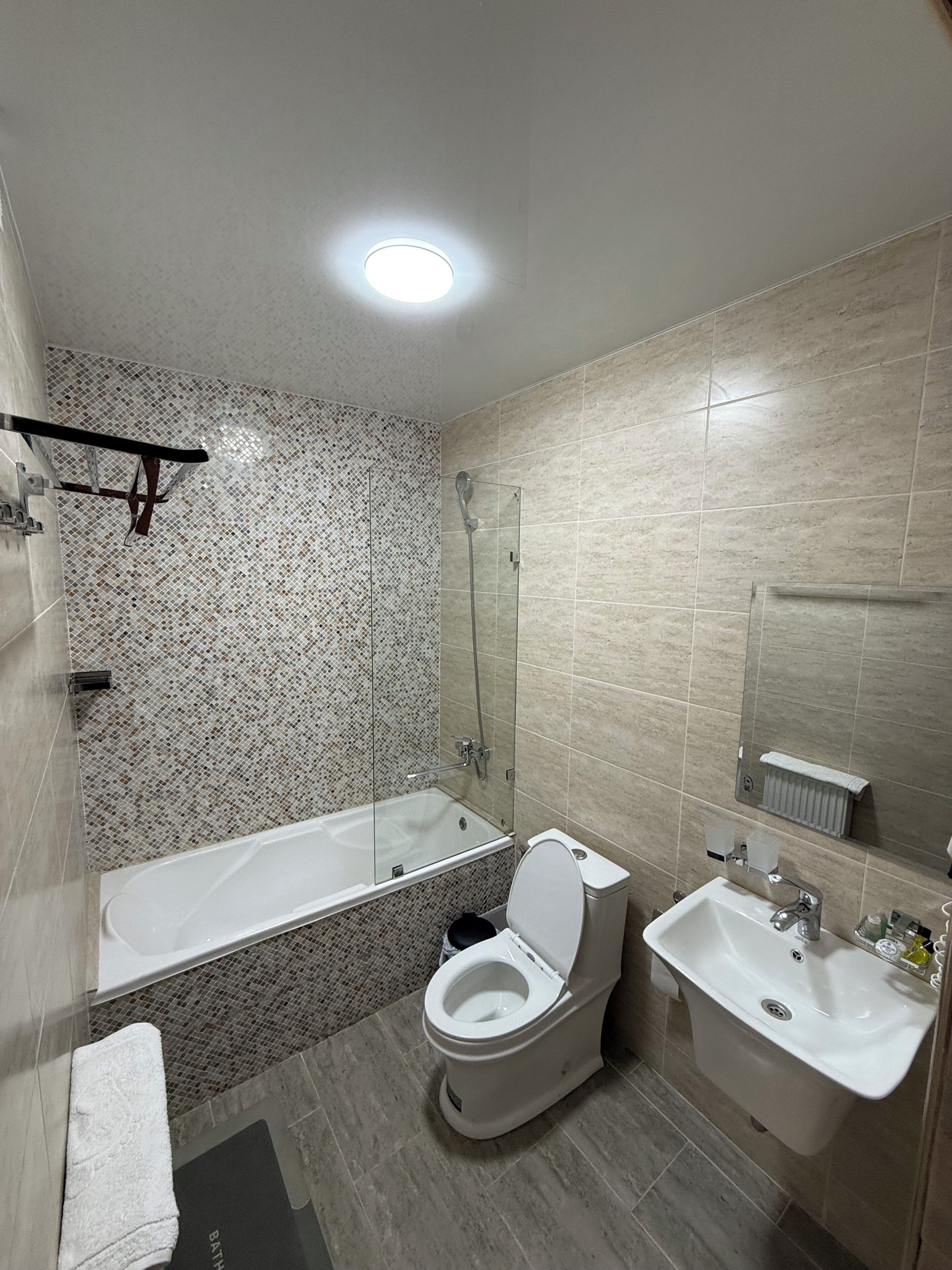 Een moderne badkamer met een badkuip, toilet en wastafel, met een betegelde muur en een plafondlamp.