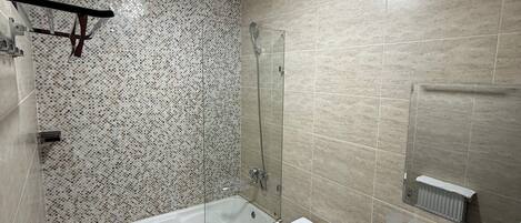 Een moderne badkamer met een badkuip, toilet en wastafel, met een betegelde muur en een plafondlamp.