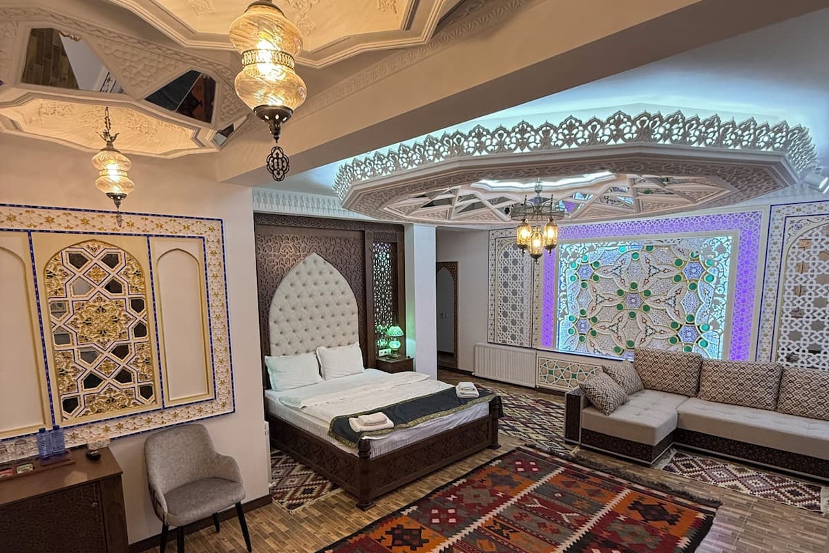 A luxurious bedroom with a large bed, a sofa, a patterned rug, and ornate ceiling details.