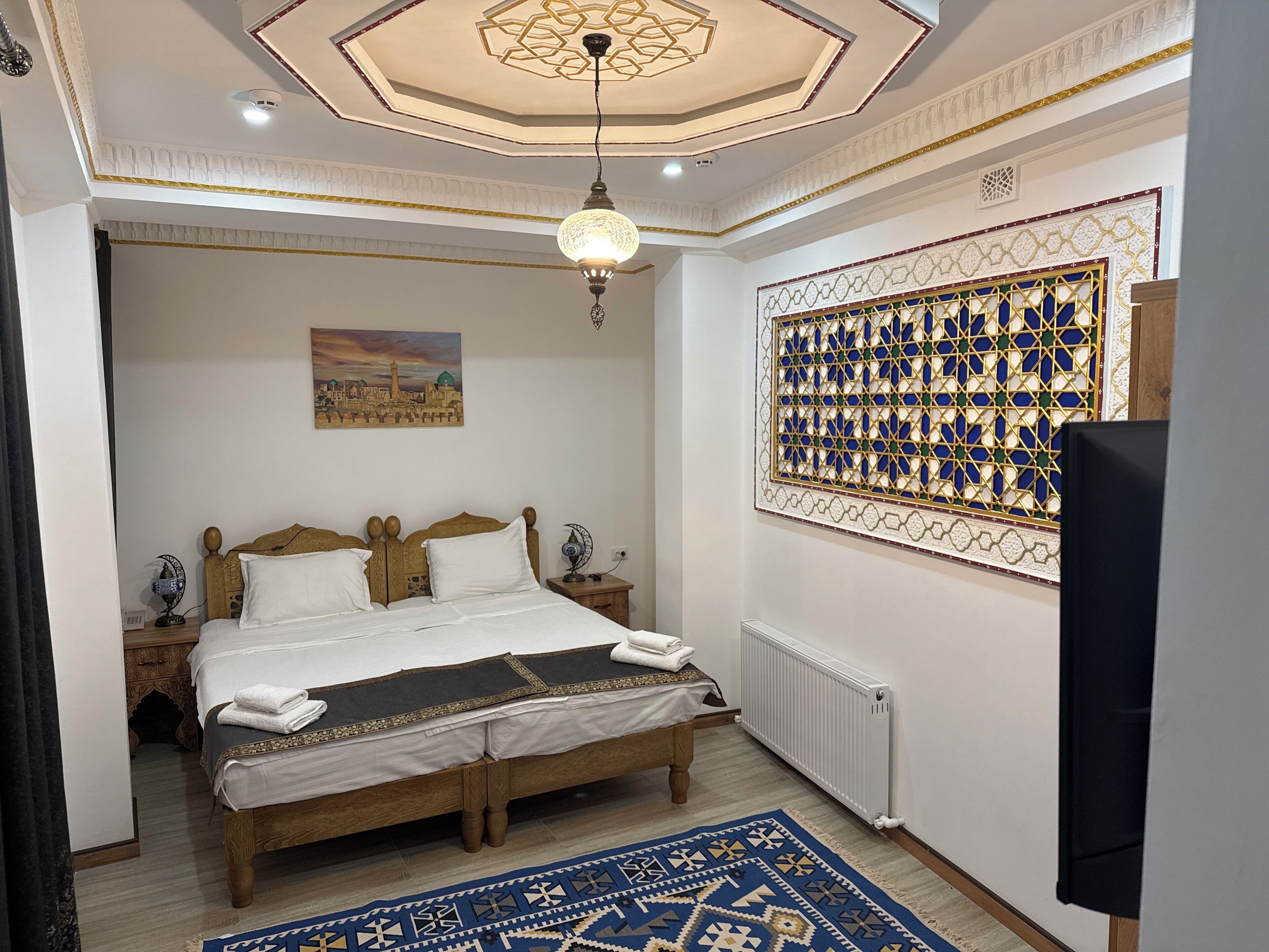 A bedroom with a wooden bed, a decorative ceiling, a patterned wall, and a nightstand with a lamp.