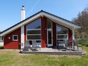 En röd byggnad med stora fönster, en terrass med stolar och en skorsten.