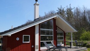 A red building with a chimney, large windows, and a deck with chairs. - 4 Star Holiday Home in Grossenbrode (Grossenbrode)