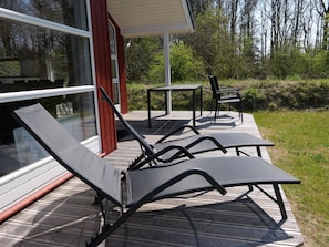 En uteplats med utemöbler, inklusive solstolar och ett bord, som ligger intill en byggnad med stora fönster.