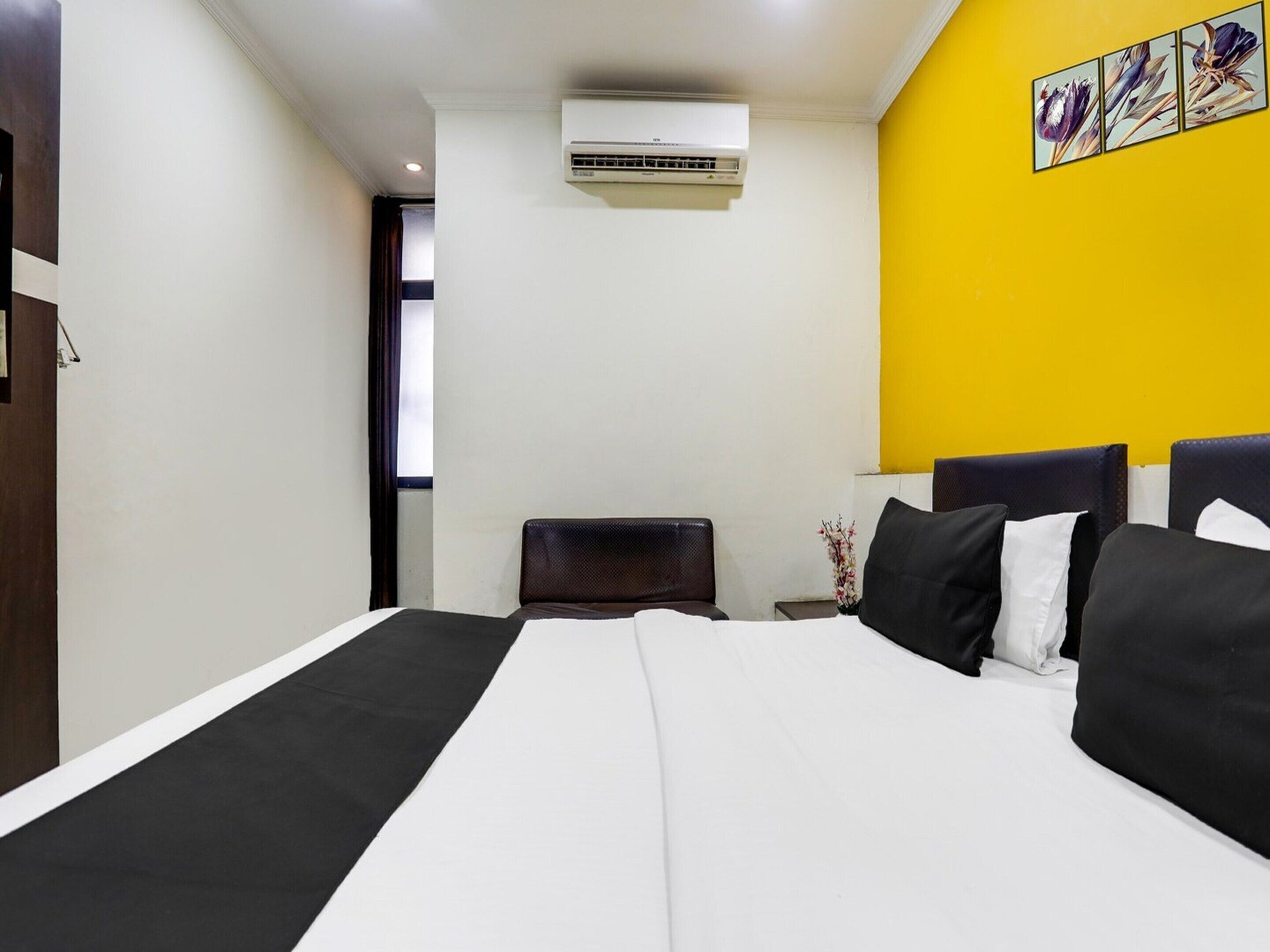 Une chambre d’hôtel avec un lit, une table de chevet, un climatiseur et un mur jaune.