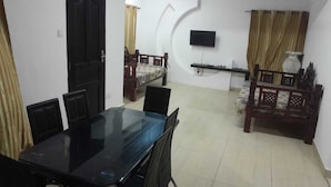 Una habitación con una mesa de comedor, sillas, una cama, un televisor montado en la pared y un ventilador de techo.