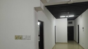 Un pasillo con paredes blancas, suelo de baldosas y techo con vigas a la vista.