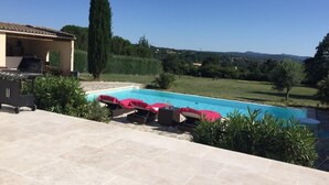 Une piscine avec des chaises longues, un barbecue et un grand arbre en arrière-plan.
