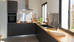 Une cuisine moderne équipée d’un four encastré, d’une cuisinière, d’un évier et d’une fenêtre laissant entrer la lumière naturelle.