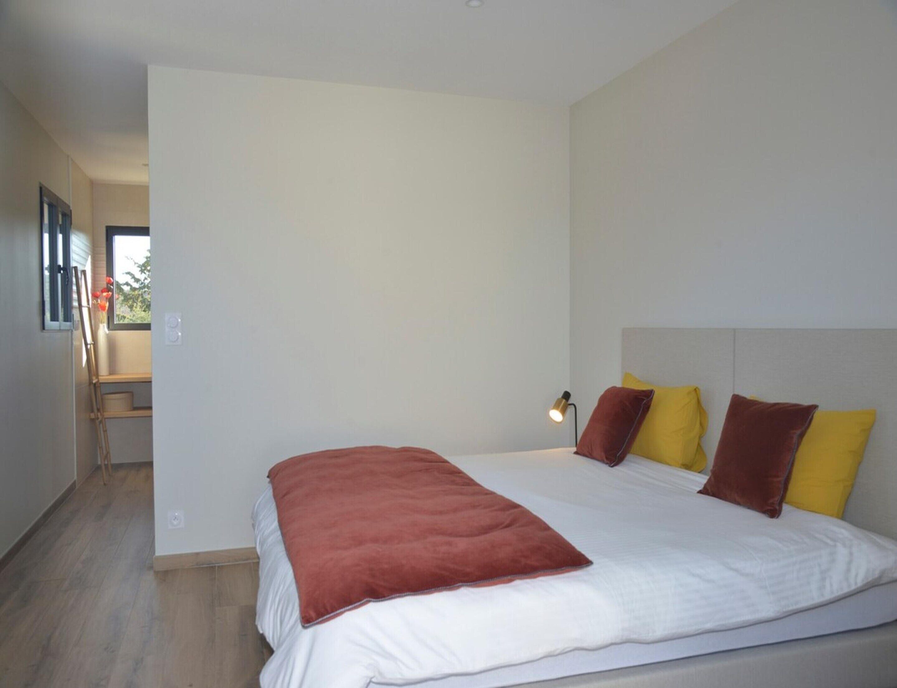 Un dormitorio con cama, mesita de noche, lámpara y ventana.