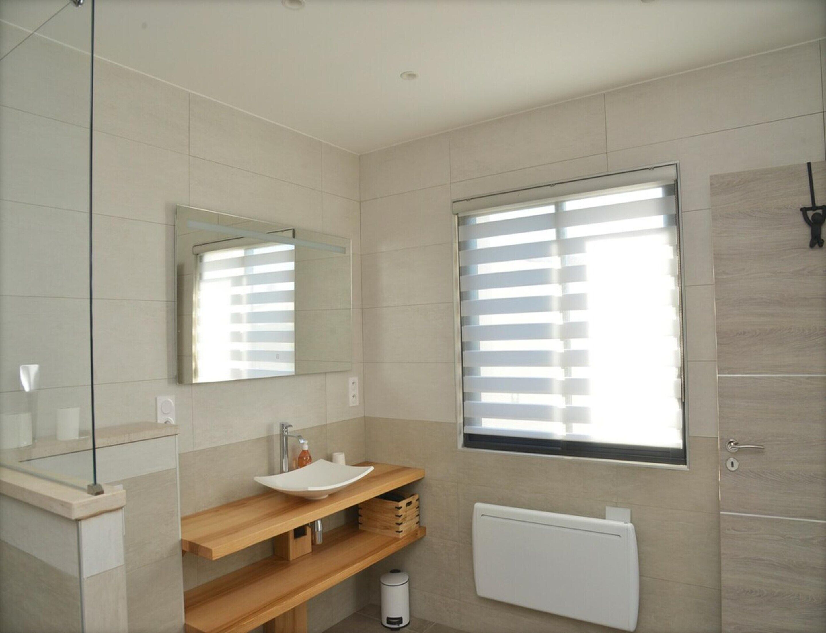 Uma casa de banho moderna com um espelho grande, uma pia branca e uma janela com persianas.
