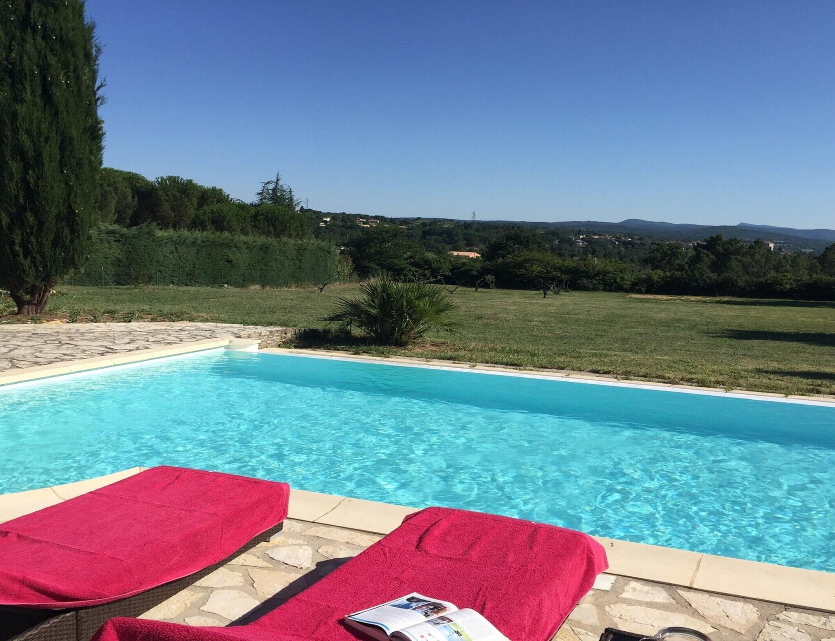 A swimming pool with two sun loungers, one with a magazine on it, surrounded by a stone deck.