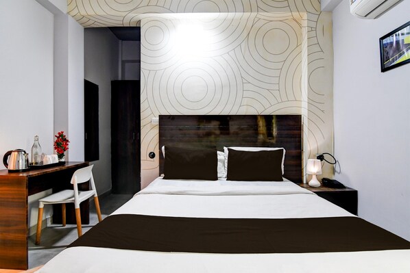 A hotel room with a bed, a desk, a chair, a nightstand, and a wall with a circular pattern.