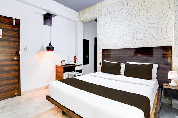 A modern hotel room with a large bed, a desk, a chair, a nightstand, and a wall with a circular pattern.