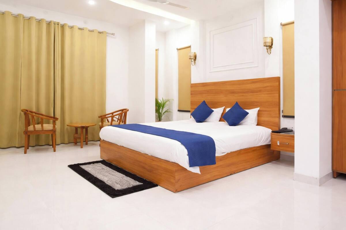 Une chambre d’hôtel avec un lit en bois, deux chaises, une petite table, une table de chevet et une plante.