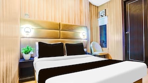 A modern hotel room with a large bed, a bedside table with a lamp, a potted plant, and a wooden headboard. - Deluxehotel Riash (Prayagraj)