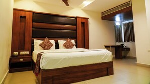 Ein Schlafzimmer mit hölzernem Bettgestell, Deckenventilator, Schreibtisch und einem Fenster mit Vorhängen.