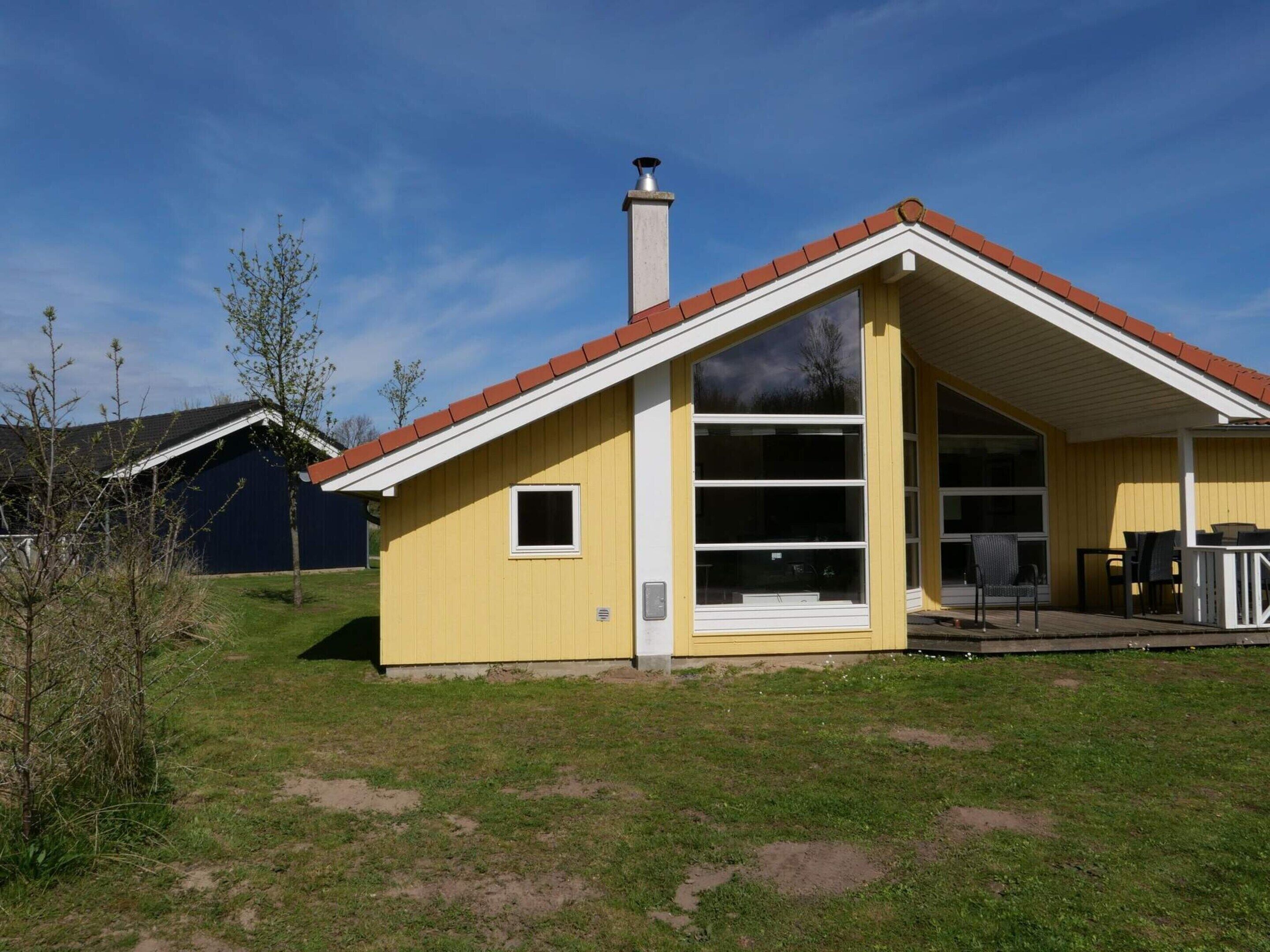 A yellow building with a red roof, a chimney, and a large window.
