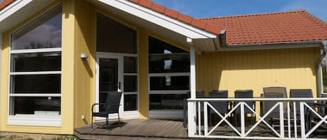 En gul bygning med en overdækket veranda, store vinduer og et hvidt gelænder.