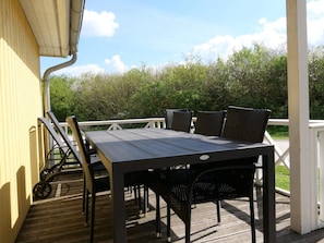 Eine überdachte Terrasse im Freien mit Tisch und Stühlen, einem Geländer und Blick ins Grüne.