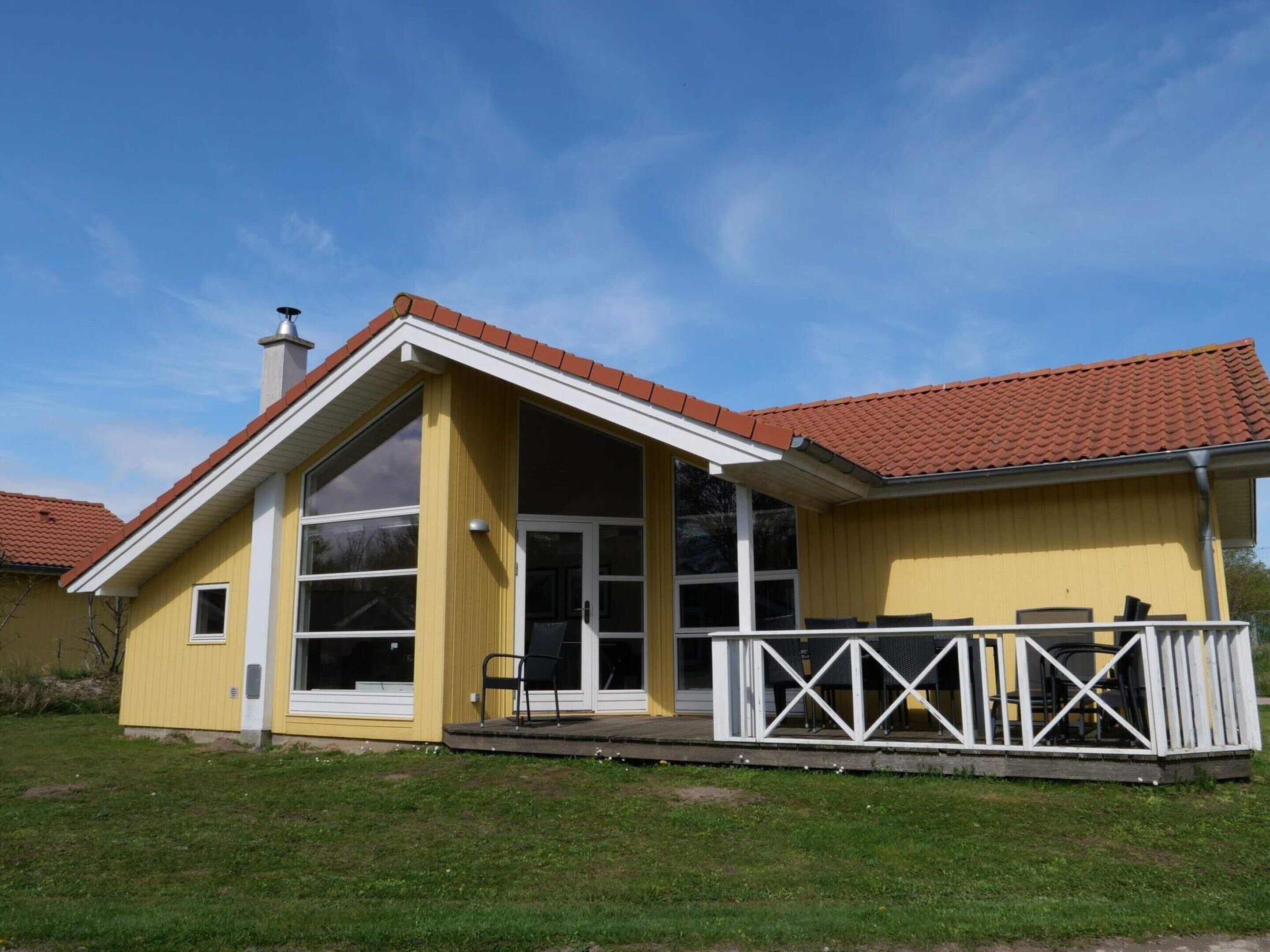 Ein gelbes Gebäude mit rotem Ziegeldach, großen Fenstern und einer Veranda mit weißen Geländern.
