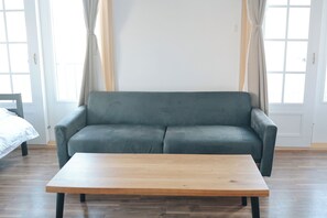 Una habitación con un sofá gris, una mesa de centro de madera y una cama con ropa blanca.