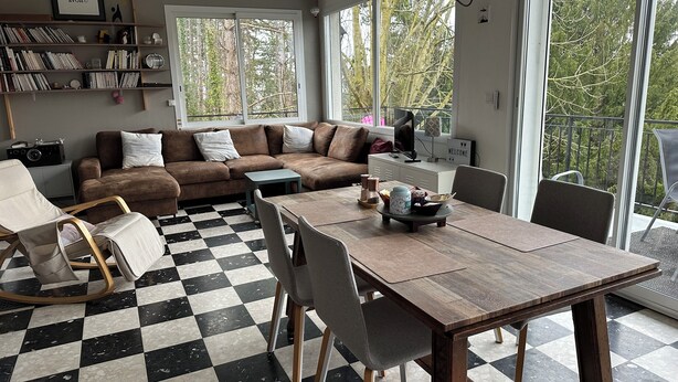 A living room with a checkered floor, a brown sofa, a wooden dining table, and a bookshelf. - Architect's house in the countryside (Sainte-Geneviève-lès-Gasny)
