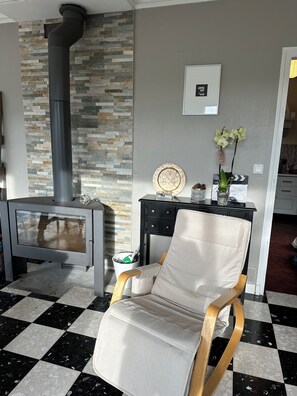 A room with a checkered floor, a stone wall, a black chimney, a modern chair, a small table with a vase of flowers, and a framed picture on the wall. - Architect's house in the countryside (Sainte-Geneviève-lès-Gasny)