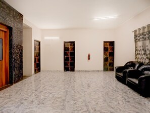 A spacious room with a marble floor, two doors with glass panels, a fire extinguisher, and a black leather sofa.
