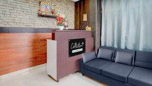 Zona de recepción con pared de ladrillo, panel de madera, mostrador de recepción con un letrero, sofá y cortina.