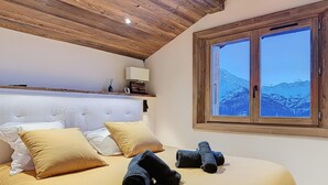 Quarto com teto de madeira, uma cama grande com roupa de cama amarela, duas almofadas e duas toalhas enroladas.