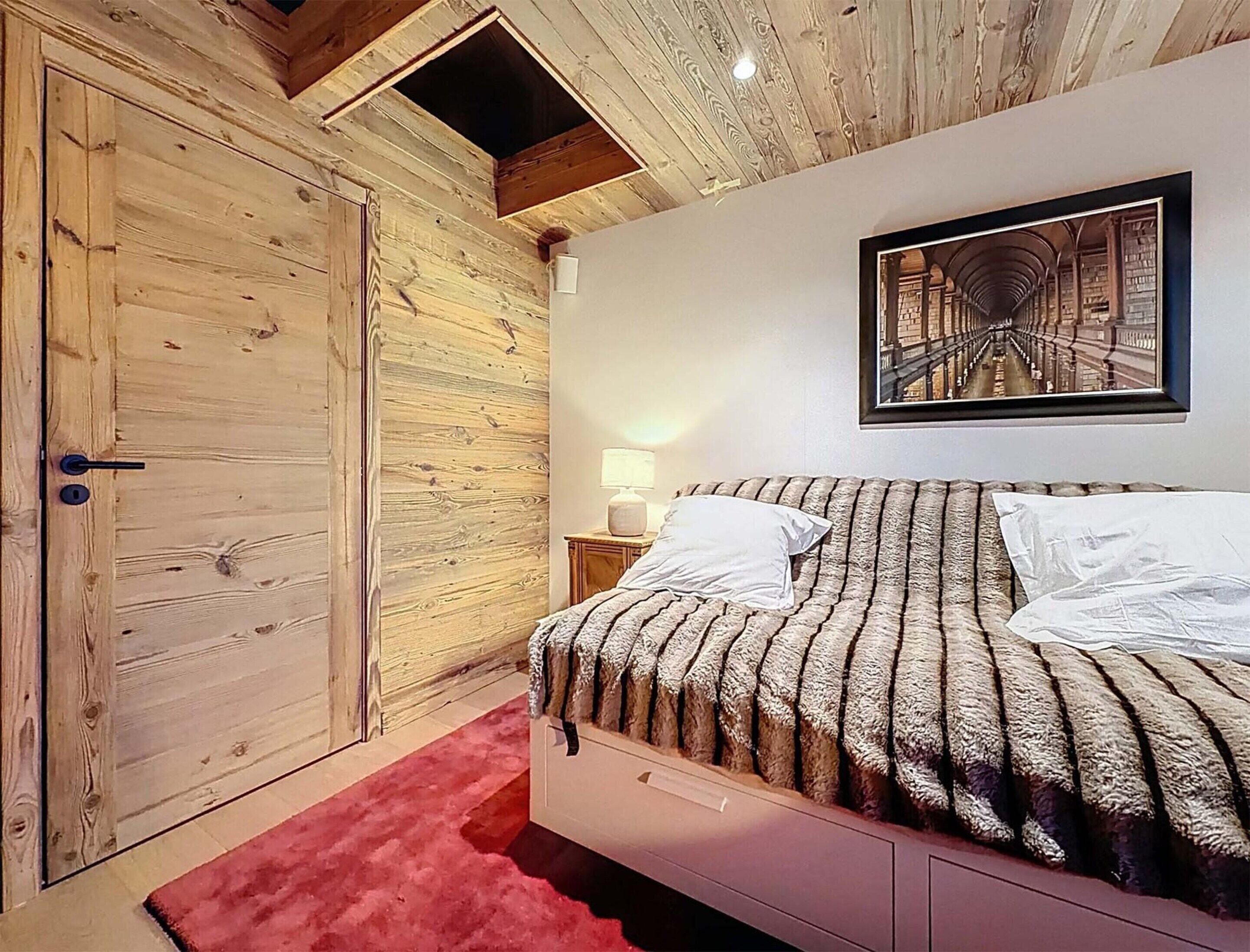 A bedroom with a wooden door, a bed with striped bedding, a nightstand with a lamp, and a framed picture on the wall.