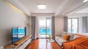 A modern hotel room with a flat-screen TV, a sofa, a coffee table, and a balcony with a view. - Tyms High Serviced Residence Shanghai Stadium Metro (Shanghai)
