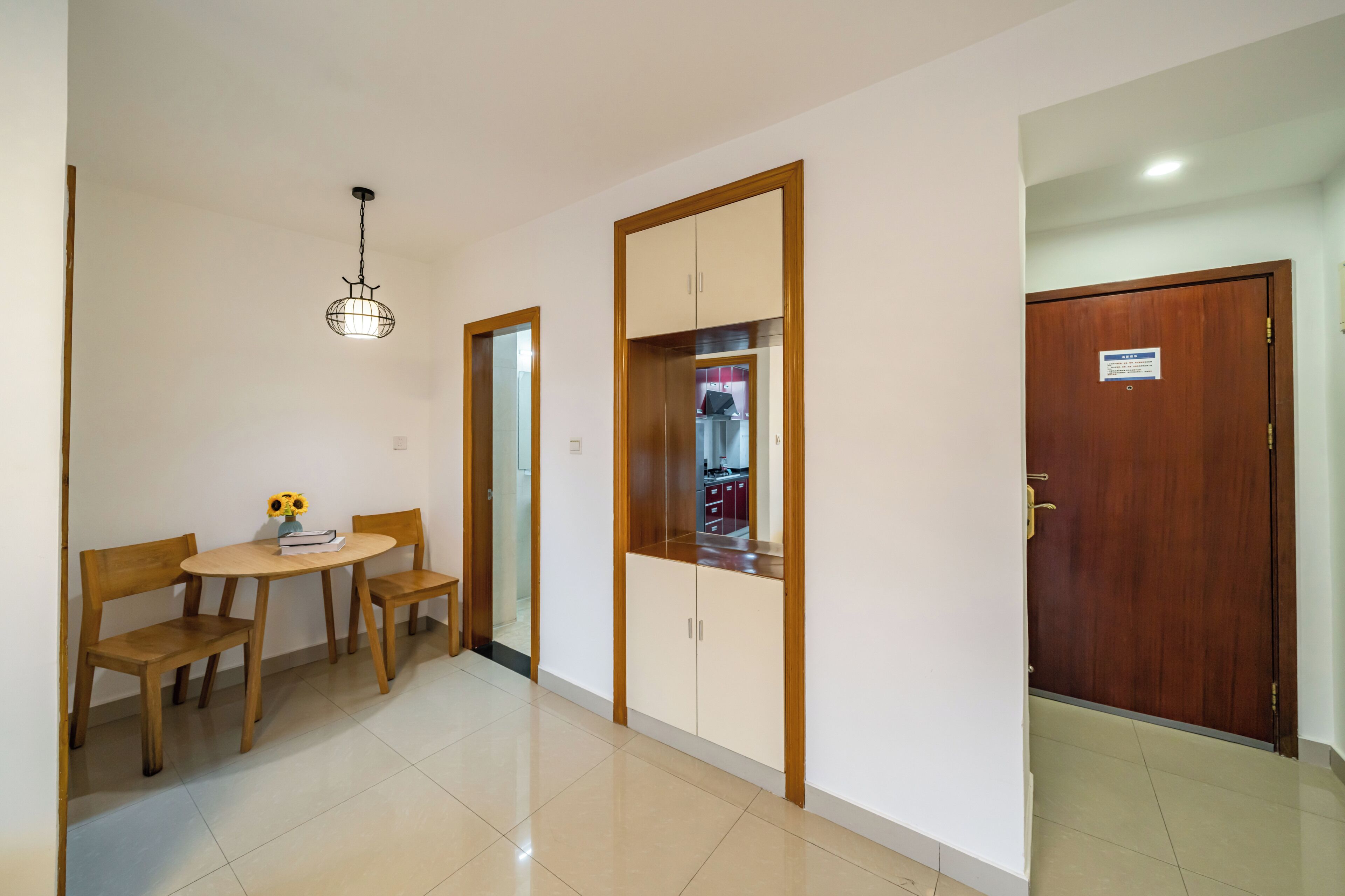 Una habitación con una mesa y sillas de madera, una lámpara colgante, un armario y una puerta con un letrero.