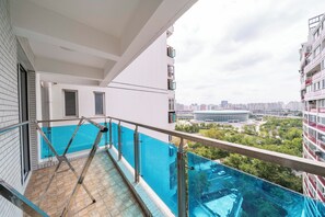 Ein Balkon mit Glasgeländer mit Blick auf einen Pool und die Stadtlandschaft.