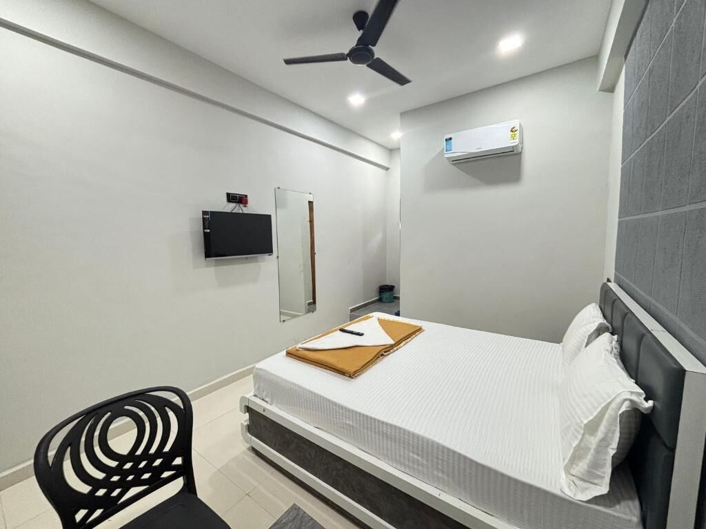 A modern hotel room with a bed, a ceiling fan, a mounted air conditioner, and a TV on the wall.